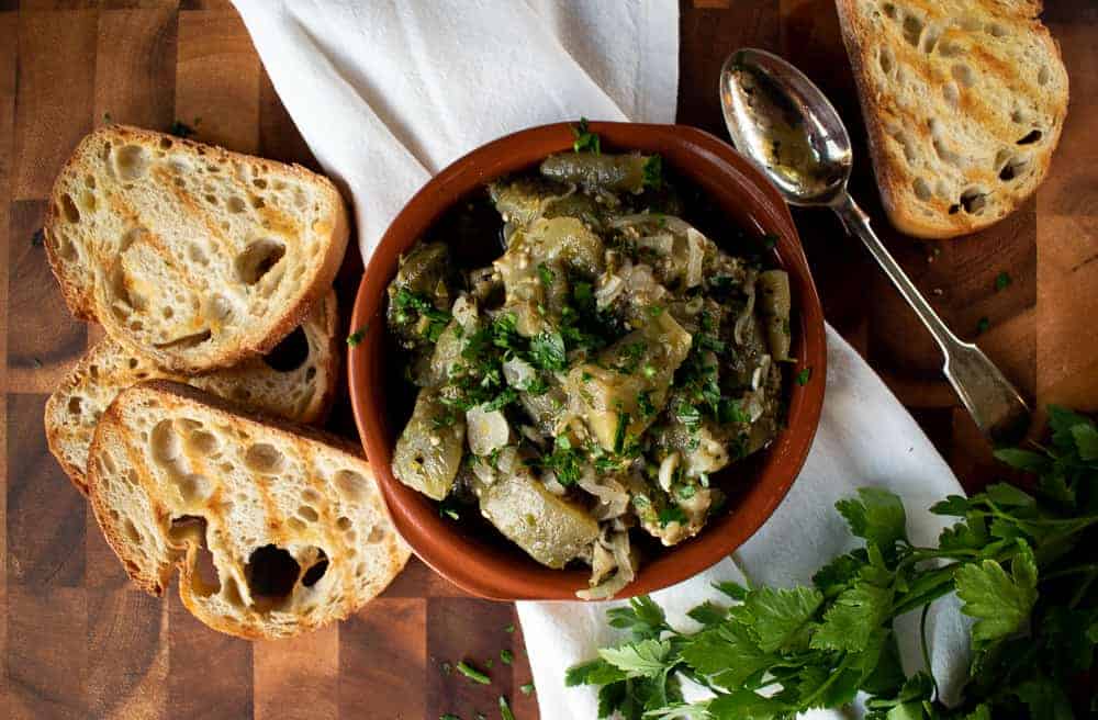 terracotta bowl filled with pickled pale green vegetables, toasted bread on the side.