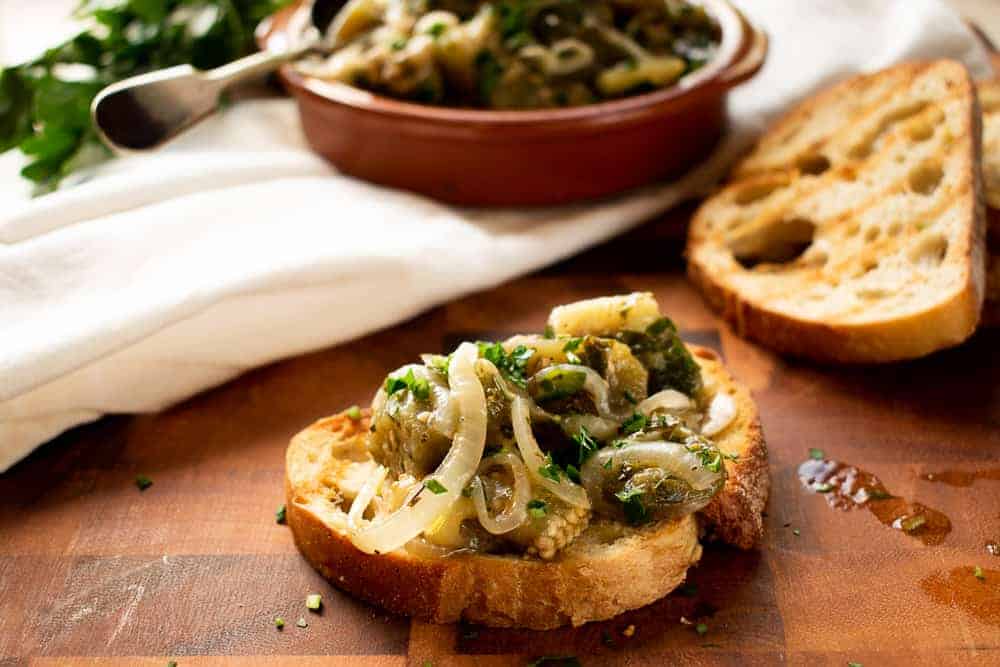 pale green strips of pickled vegetable on toasted bread with extra in the background.