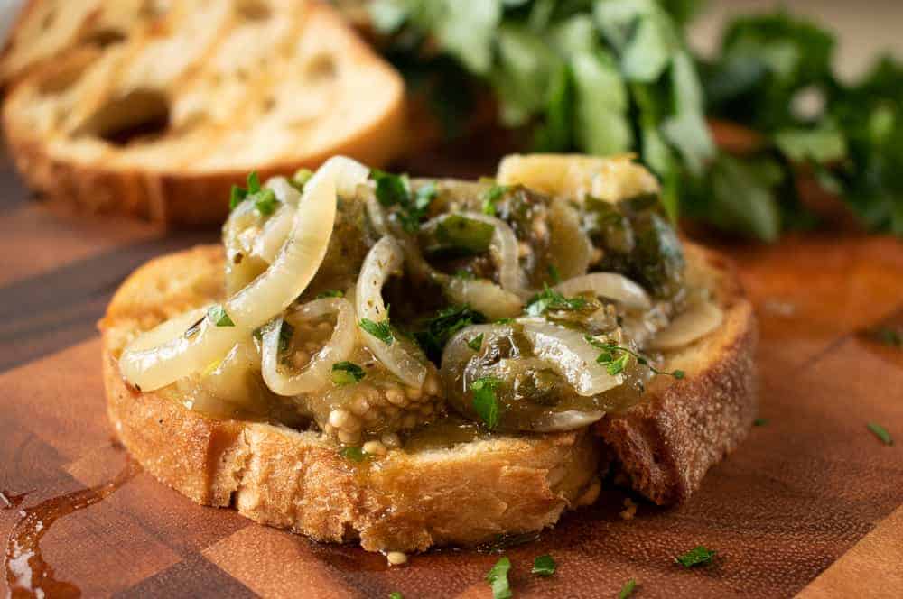 Oregano Marinated eggplant on bread with parsley and bread in the background.