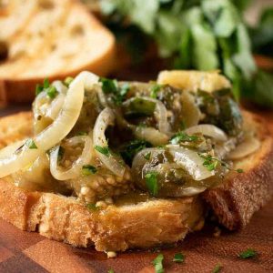 close up of pale green strips of pickled vegetable on toasted bread with extra in the background.