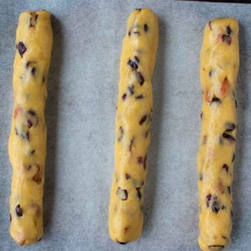 Logs of dough specked with cranberries on baking paper.