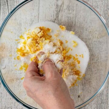 Fingers rubbing orange zest into sugar.