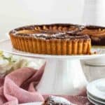 Chocolate almond pear tart on a white cake stand with a slice removed and plated in front.