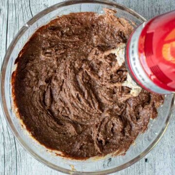 Brown creamy mixture being mixed with an electric hand held red mixer.