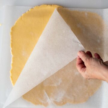 Rolled out pastry under a sheet of parchment paper with one edge of the paper being lifted.