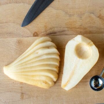 A peeled pear, cut in half and cored with one half sliced lengthwise and fanned out.