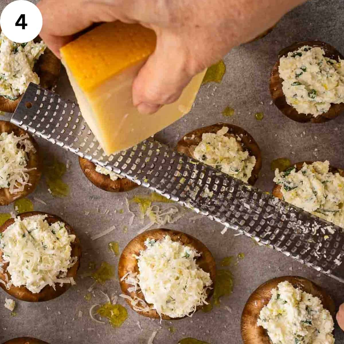 Grating a block of cheese over stuffed mushrooms.