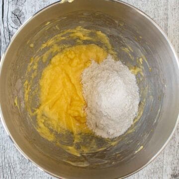 Pale yellow creamy mixture in bottom of steel bowl and a pile of flour on top.