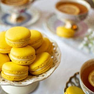 Lemon Macarons on white stand with three cups of lemon tea on a white cloth