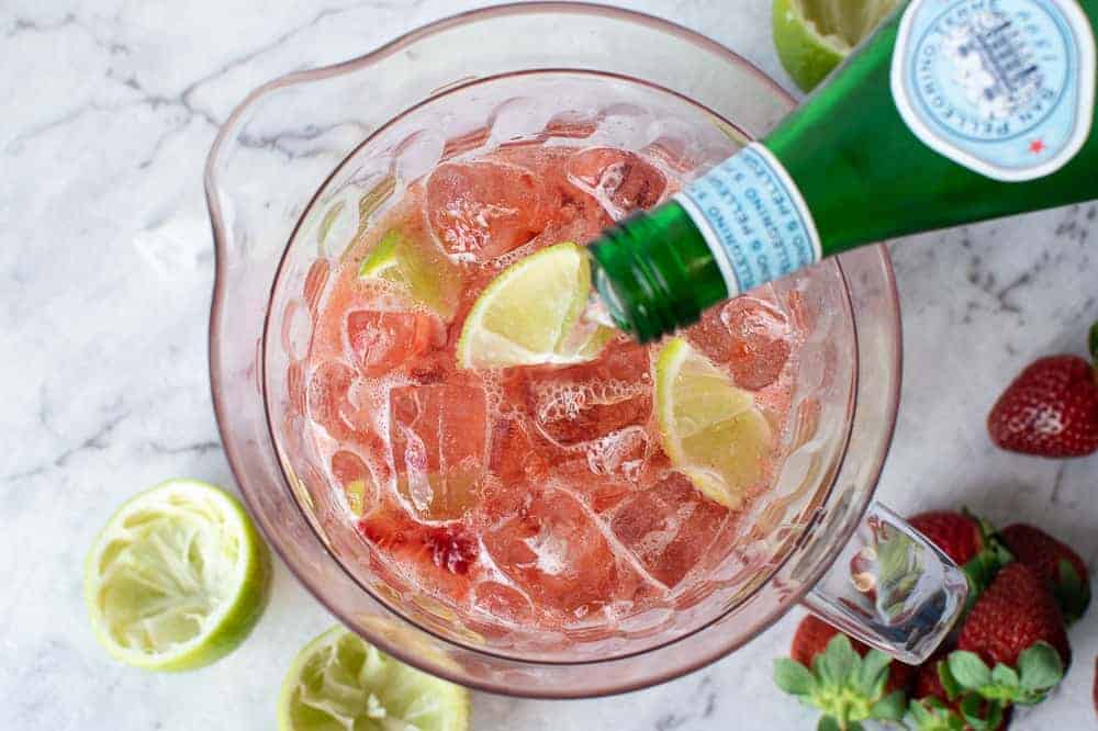 Pouring sparkling water into strawberry and lime in a clear jug
