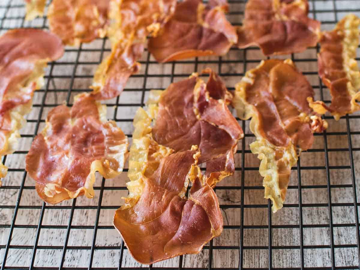 Cooked prosciutto slices on a black wire rack.