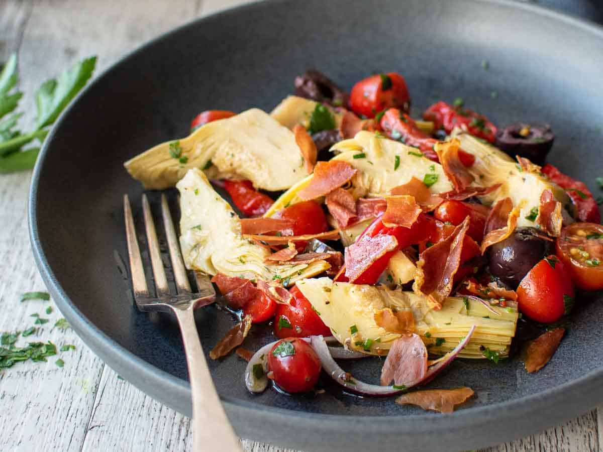 Salad of artichokes and other vegetables in a dark shallow bowl with a fork