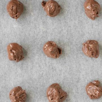 Blobs of Nutella spread on a parchment lined baking sheet.