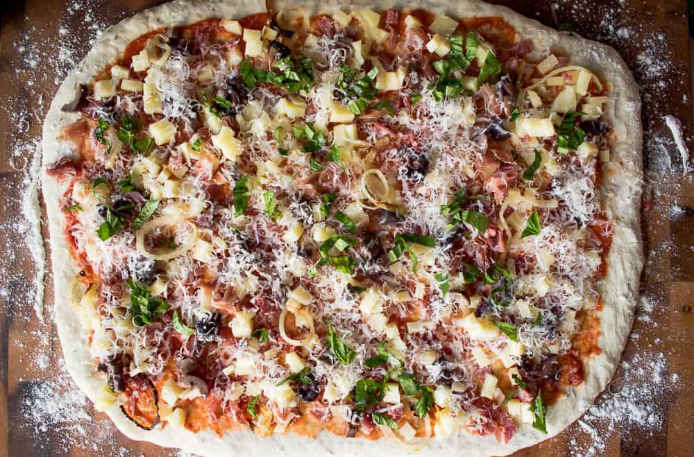 Bread dough rolled into oblong shape topped with pizza sauce, cheese, prosciutto, salami and basil.
