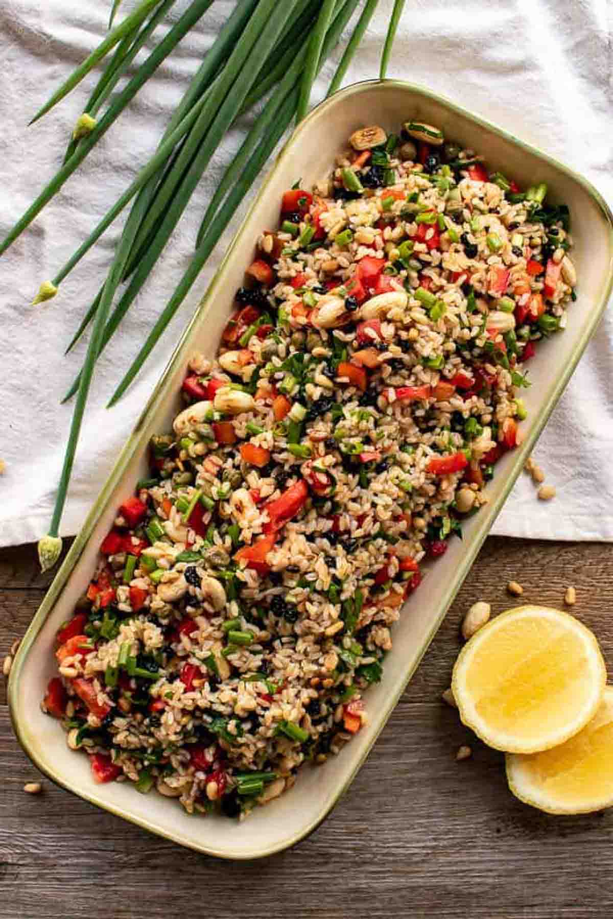 Brown rice salad in oblong plate with spring onions and lemon.