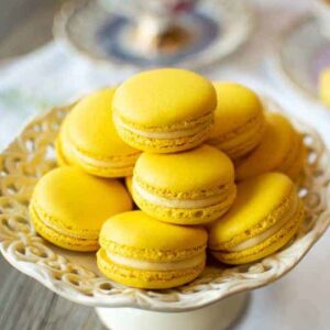 Lemon Macarons on white stand with three cups of lemon tea on a white cloth.