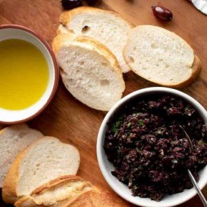 bowl of olivada with bread, oil and parsley on wooden board