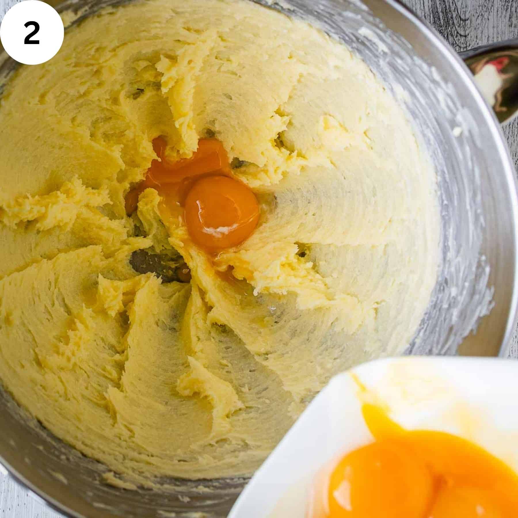 Egg yolks being added to creamy butter  mixture in a bowl.