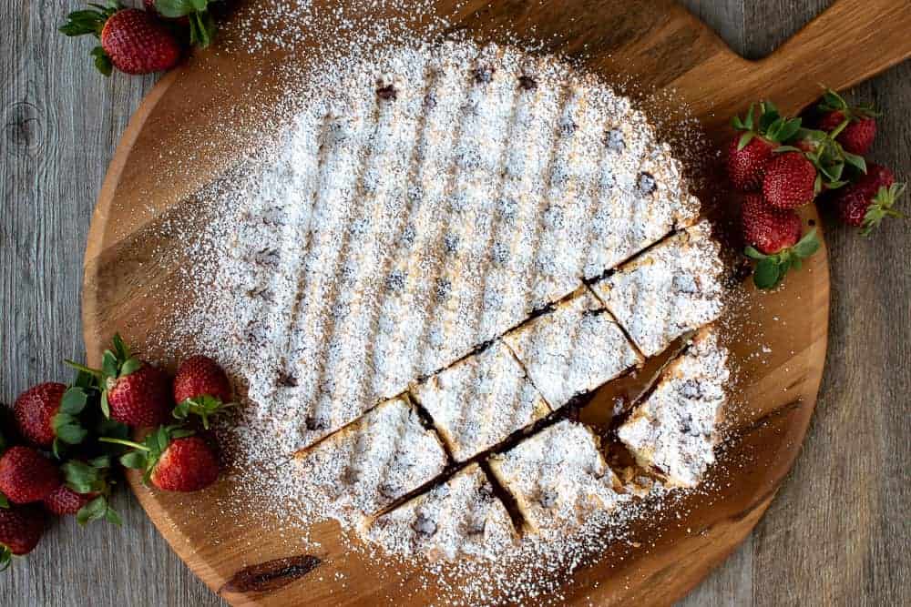 Strawberry crostata recipe dusted with powdered sugar with a few squares cut.