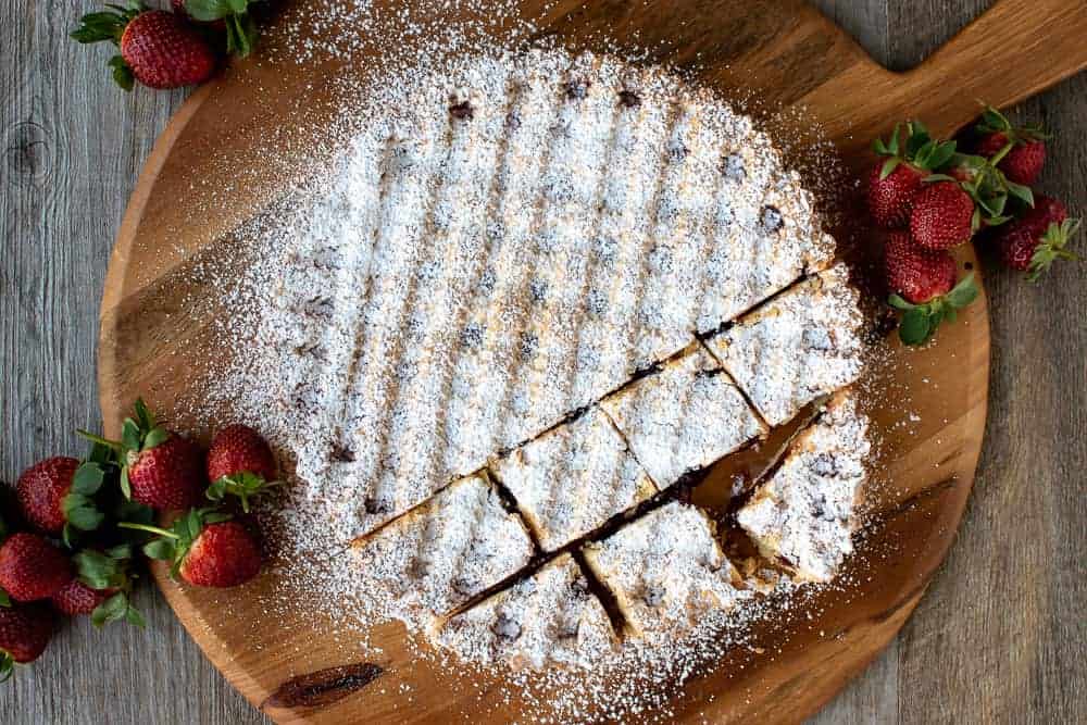 This Strawberry Crostata recipe | Easy Strawberry Tart is an easy Italian pastry filled with fruity jam #strawberrycrostata #crostatarecipe #strawberrytart #crostatadough Strawberry crostata recipe dusted with powdered sugar with a few squares cut.