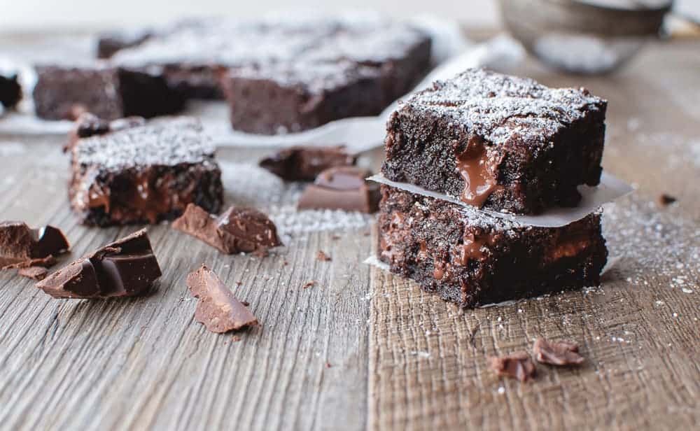 Dark chocolate brownies cut into squares with two stacked on top of each other and chocolate scattered around.