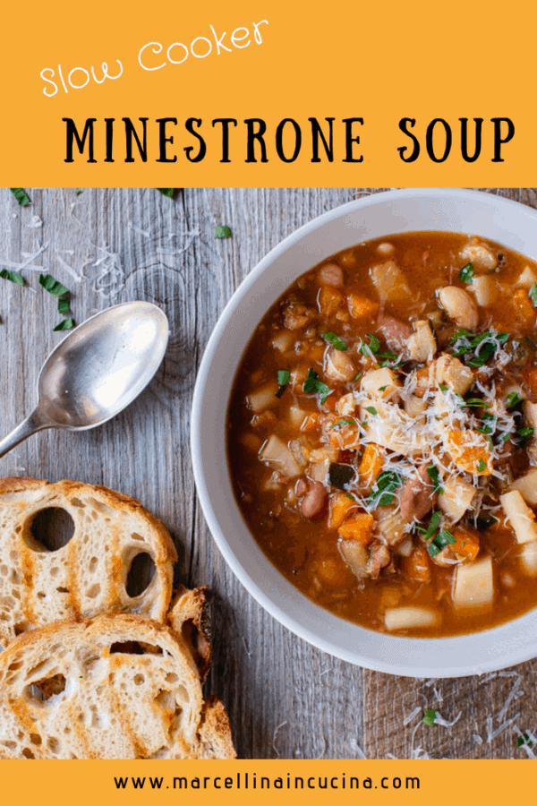 White bowl of slow cooker minestrone soup, two slices of toasted bread and spoon on wooden table