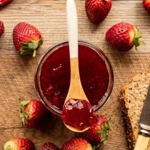 Jar of jam with strawberry jam on a spoon. strawberries and bread.
