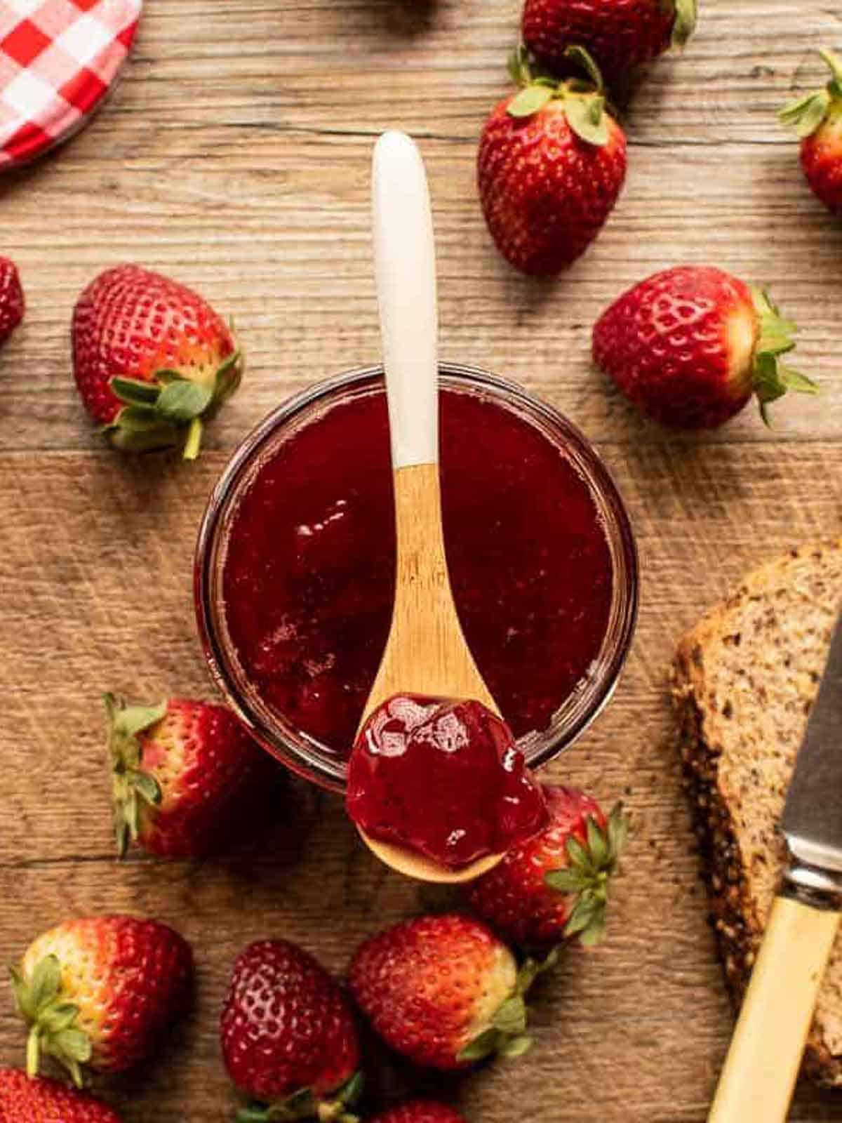 A jar of the finished strawberry jam recipe with a spoon of the jam resting on top. 