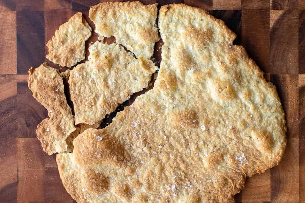 Large round cracker partly broken into serving pieces on a wooden table