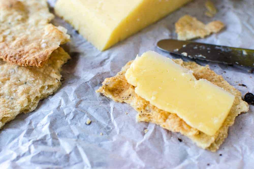 A cracker with cheese on top on baking paper.
