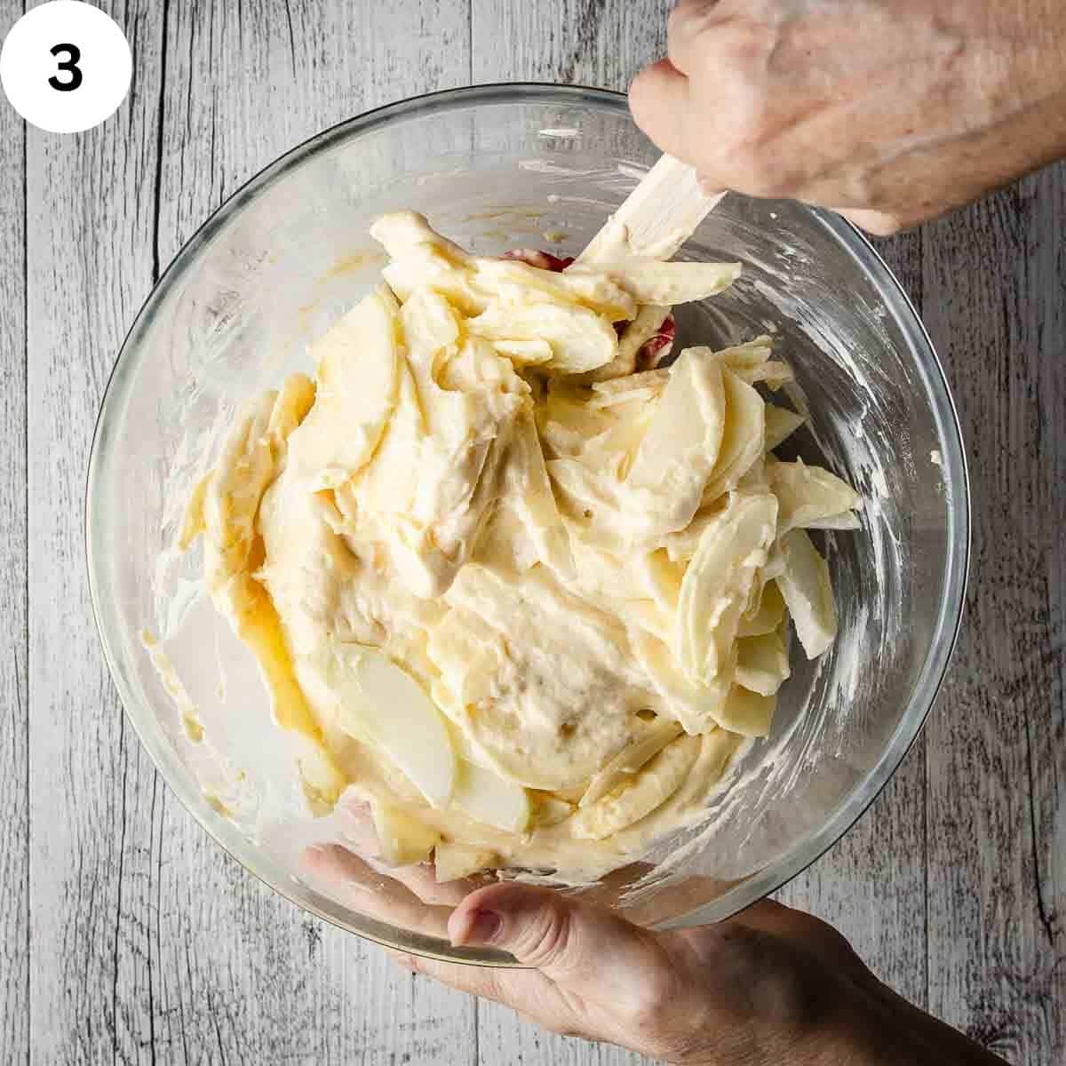 Combining apple slices with cake batter using a spatula.
