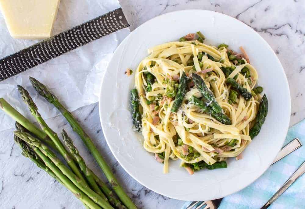 pasta with asparagus on white plate, fresh asparagus, block of cheese and grater