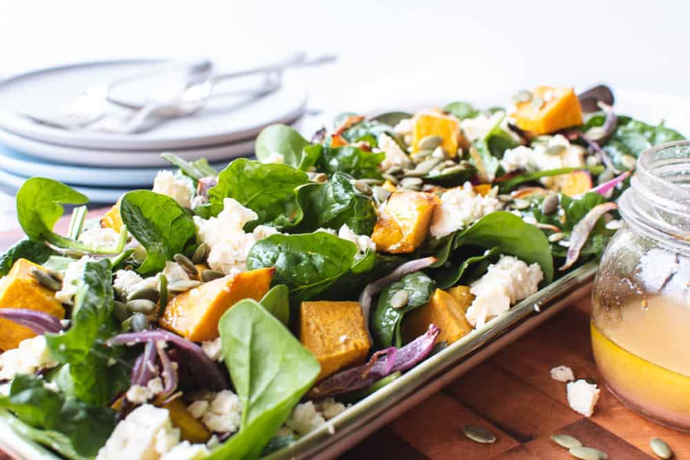 pumpkin and spinach salad on oblong plate on wooden board with plates and forks.