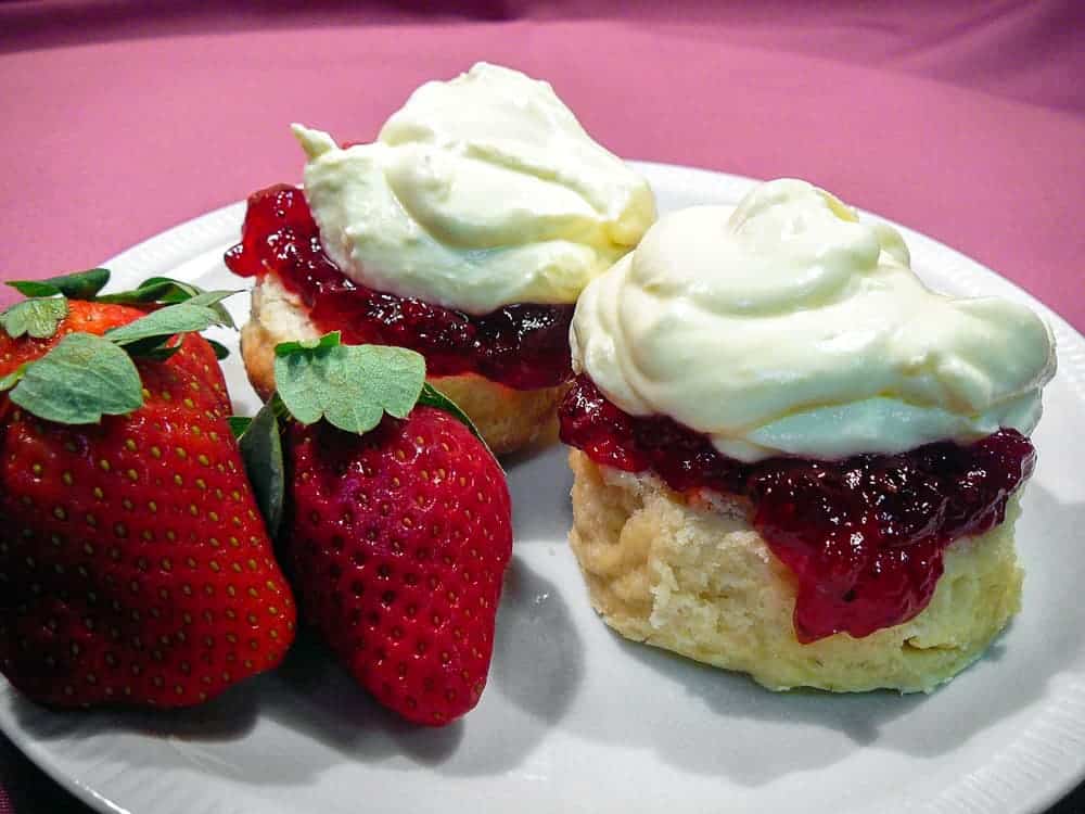 English scones split and topped with jam and cream with strawberries on the side.