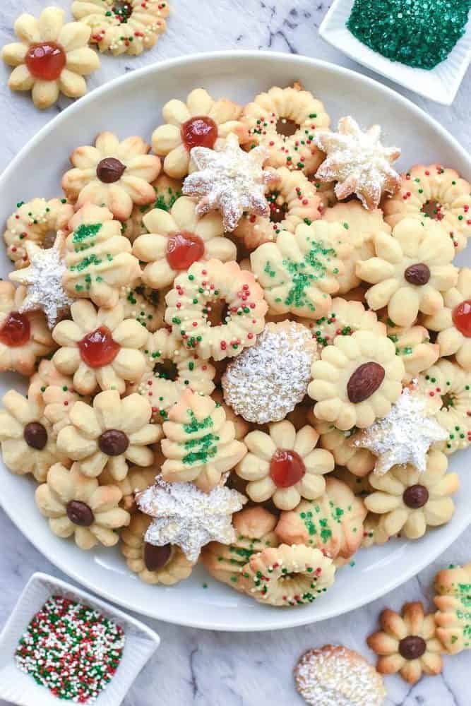 Decorated Italian butter cookies on a  white plate with two small bowls of cake sprinkles.