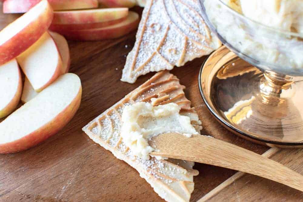 close up of creamy spread on pizzelle with apple slices on the side.