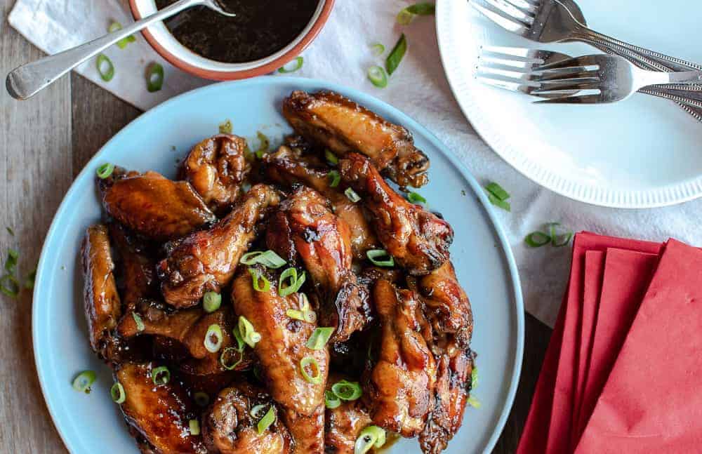 Honey baked chicken wings on blue plate with bowl of sauce with white plates, forks and red paper serviettes