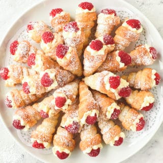 cream horns filled with cream and topped with raspberry arranged in a circular pattern on a round white plate viewed from above
