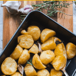 roasted potatoes in black oven tray on a wooden board