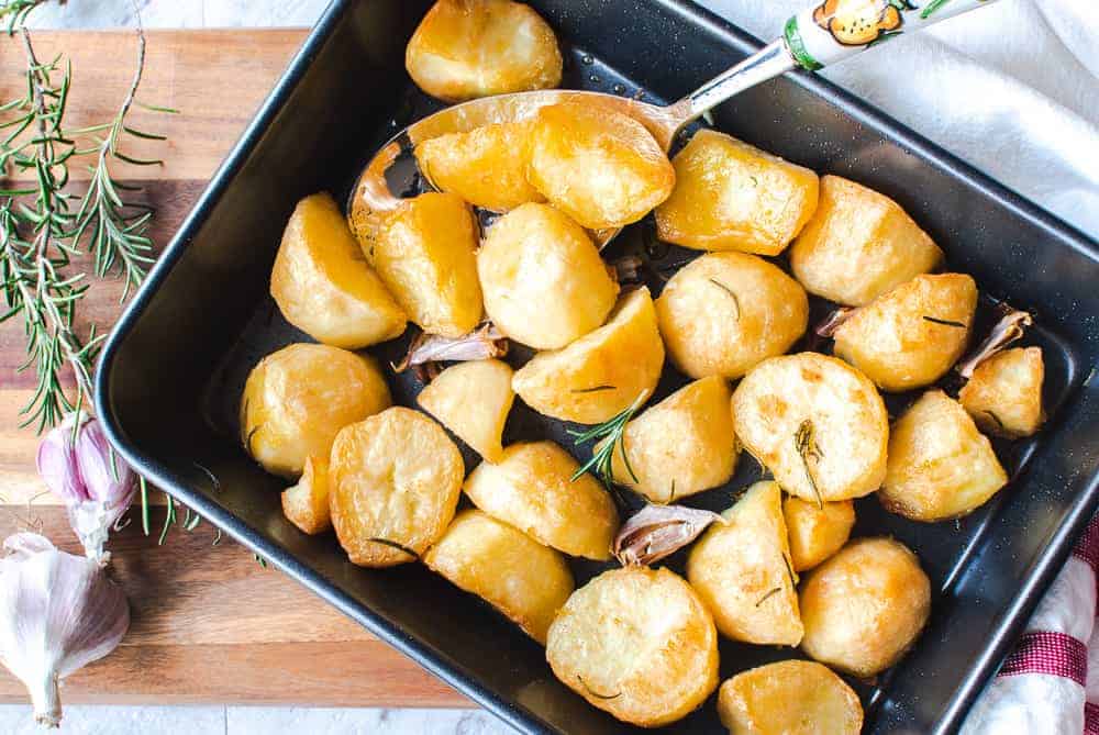 Crispy roast potatoes served in black oven tray on a wooden board