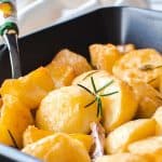roasted potatoes in black oven tray with serving spoon