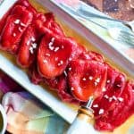 Roasted Red Peppers on cream colored platter with a drizzle of oil, anchovies and a chopped garlic