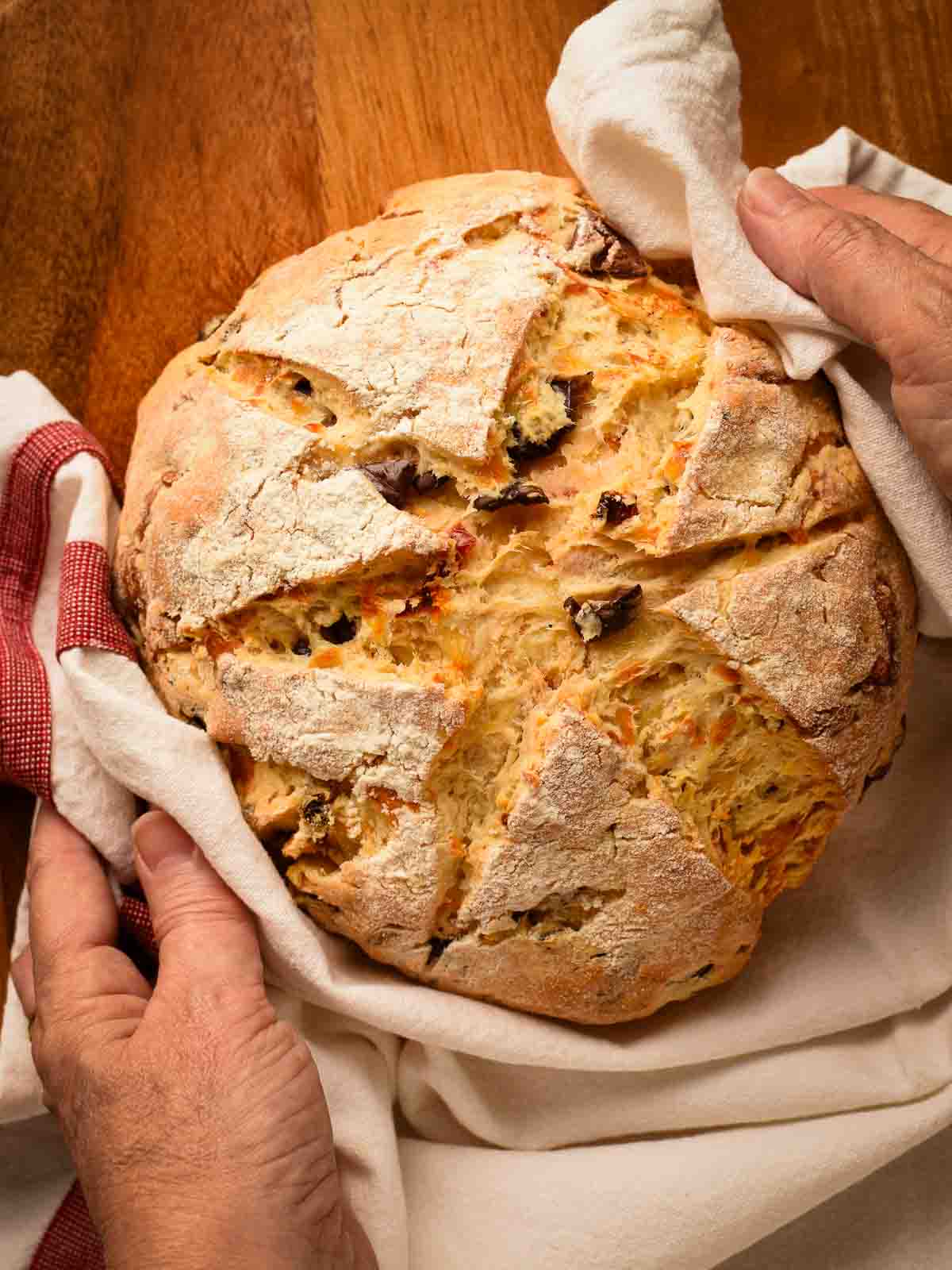 Damper with olives, sun dried tomatoes and cheese is tasty, quick and delicious #damper #quickbread #sodabread #recipe #italianfood #australianfood Italian Quick Bread wrapped in a cloth held by two hands.
