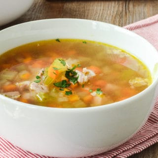 Chicken and vegetable soup in white bowl on red and white striped cloth viewed from the side