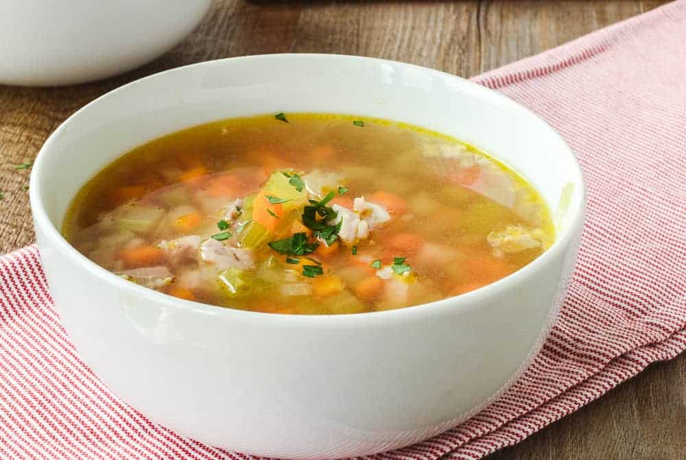 Chicken and vegetable soup in white bowl on red and white striped cloth viewed from the side