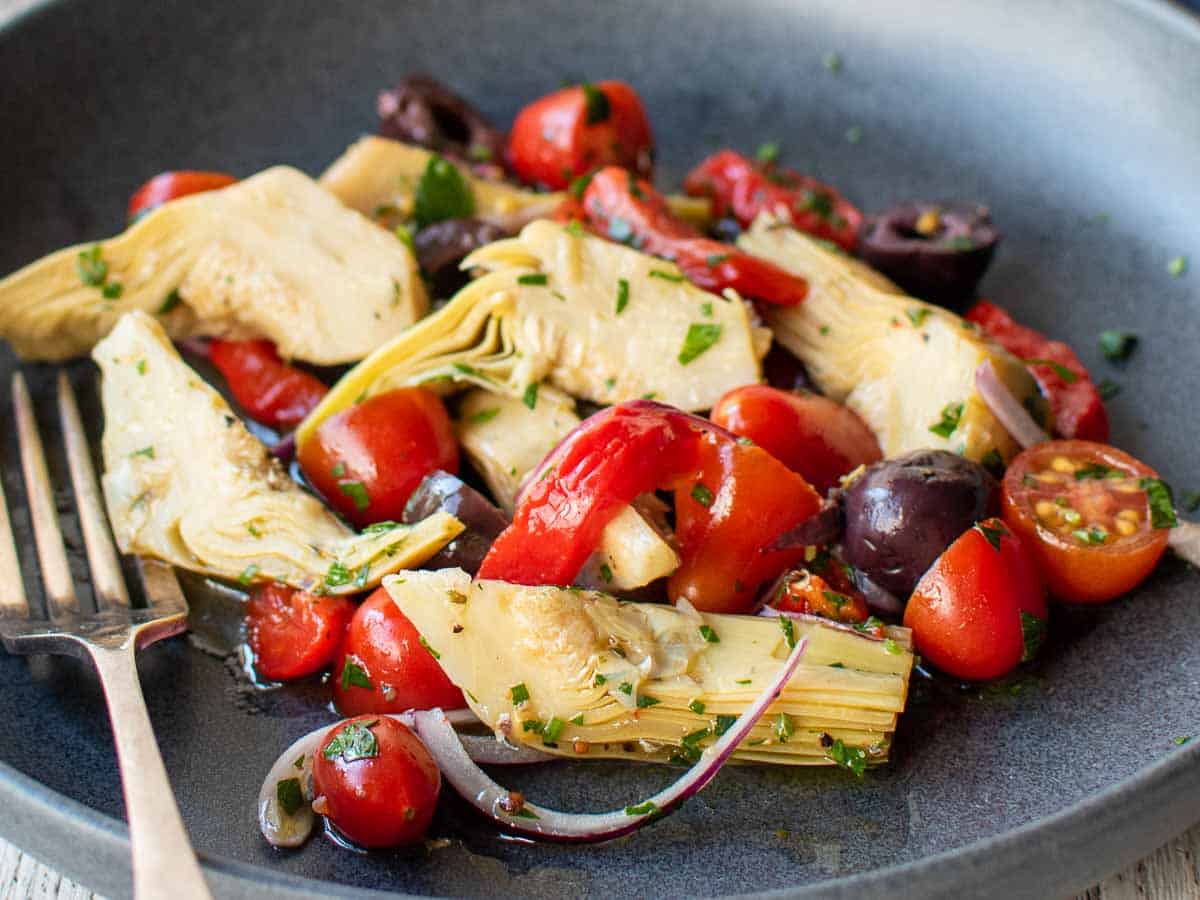 Close up of a salad with artichoke hearts and various salad ingredients in a dark colored bowl.