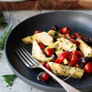 Artichoke Salad in a dark shallow bowl with a fork