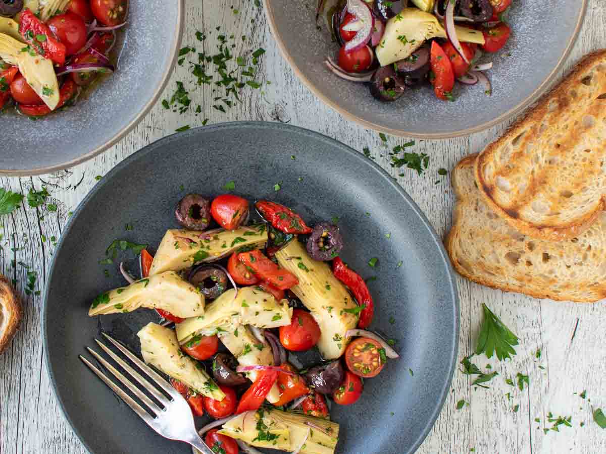 Overhead view of a salad with artichokes in a dark bowl.