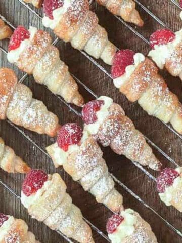 pastry horns filled with cream and topped with a raspberry on a wire rack.