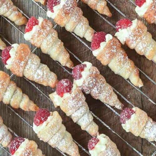 pastry horns filled with cream and topped with a raspberry on a wire rack.
